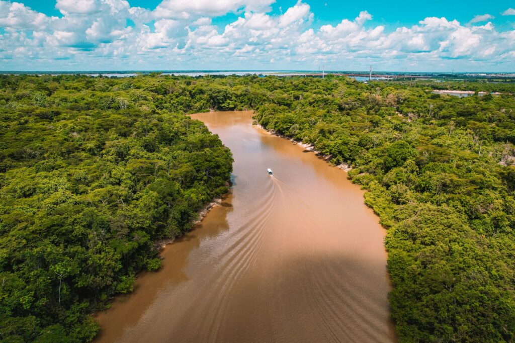A scenic aerial shot of a boat navigating through the muddy Amazon River surrounded by lush rainforest.